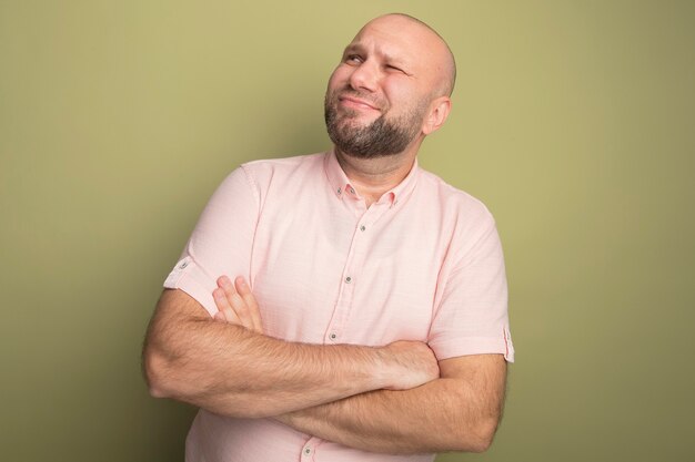 Scontento guardando l'uomo calvo di mezza età laterale che indossa la maglietta rosa che attraversa le mani isolate su verde oliva