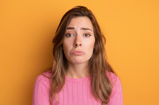 Sconvolto la giovane bella donna in top rosa che guarda la telecamera con un'espressione triste che increspa le labbra