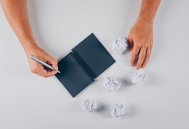 Scrittura dell'uomo di vista superiore sul blocco note con le carte sgualcite su bianco