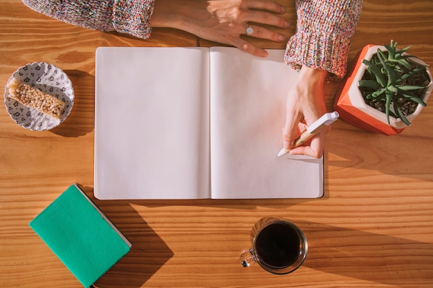 Scrittura della donna sulla penna con il taccuino bianco in bianco sopra lo scrittorio di legno