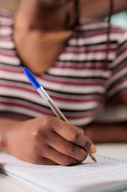 Scrittura della mano della donna afroamericana con la penna nel blocco note al primo piano della scrivania. Studente che prende appunti nella vista ravvicinata del pianificatore, studia, si prepara per l'esame, fa i compiti nel taccuino
