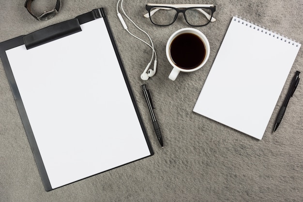 Scrivania da ufficio grigia con tazza di caffè; auricolari e occhiali
