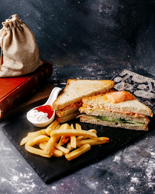 Scrivania nera del pasto di vista frontale con le patate fritte e panino sul pavimento grigio