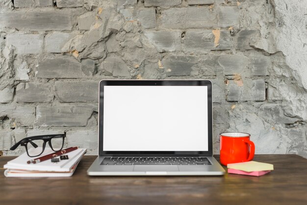 Scrivania organizzata con computer portatile; spettacolo; tazza di caffè rosso e forniture per ufficio