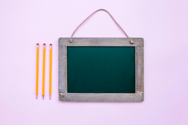 scuola ardesia con tre matite su sfondo rosa