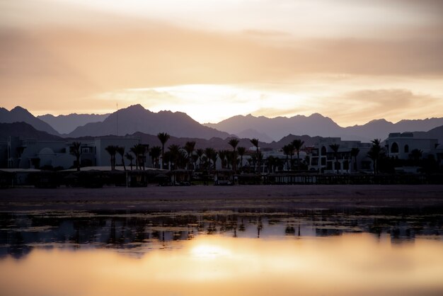 Seascape con un cielo riflettente. Il sole tramonta sulla città vicino alle montagne.