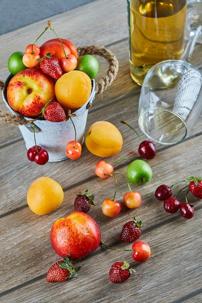 Secchio di frutta fresca estiva, bottiglia di vino bianco e bicchiere vuoto sulla tavola di legno.