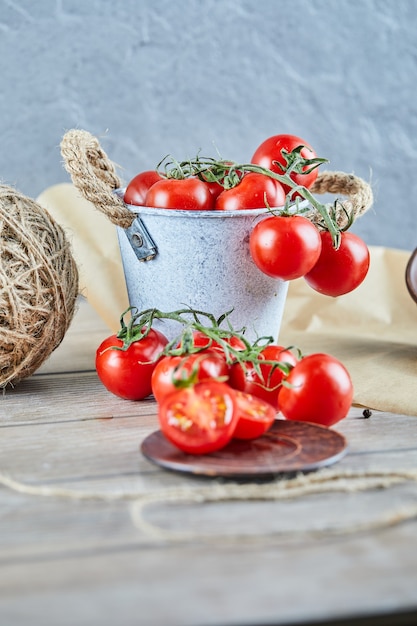 Secchio di pomodori e pomodoro tagliato a metà sulla tavola di legno.