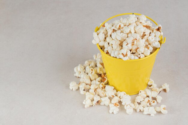 Secchio giallo troppo pieno di popcorn croccante sul tavolo di marmo.