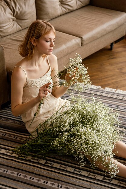 Seducente donna seduta accanto al divano mentre si tengono i fiori primaverili