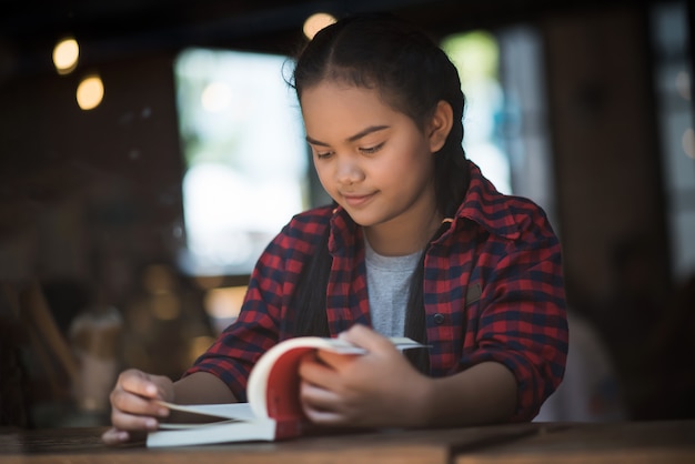 Seduta del libro di lettura della giovane donna dell&#39;interno in caffè urbano.