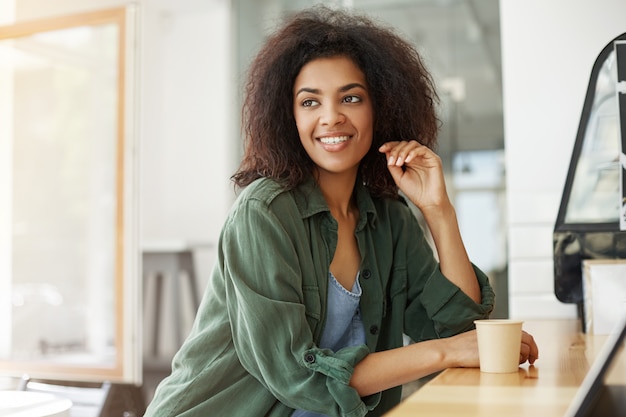 Seduta di rilassamento di riposo della giovane bella studentessa africana nel caffè bevente sorridente del caffè.