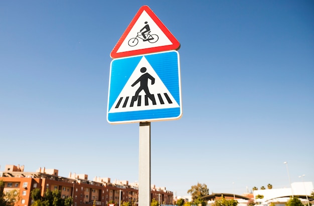 Segnale di pericolo triangolare della bicicletta sopra il segnale stradale quadrato del passaggio pedonale dentro la città