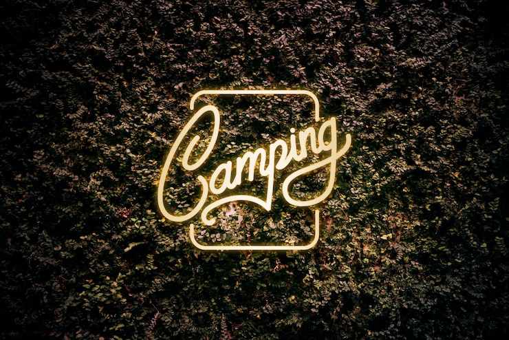 Foto gratuito segno di campeggio giallo al neon su foglie