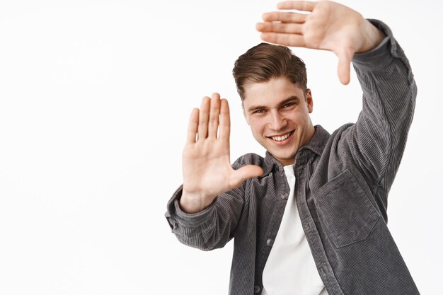 Sei bellissima. Bell'uomo sorridente che controlla qualcosa di bello, guarda attraverso i fotogrammi delle mani, immagina la scena in mente, crea, cerca l'angolo di ripresa perfetto