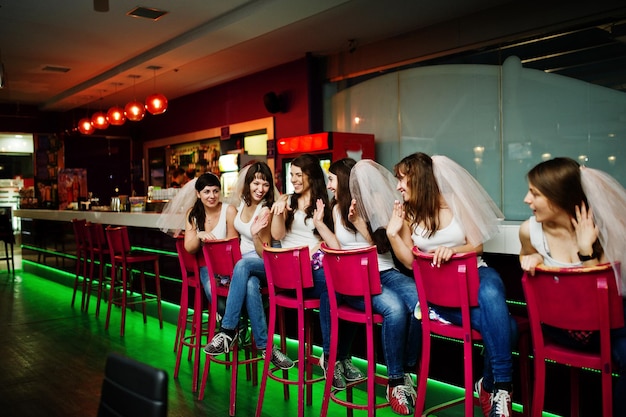 Sei ragazze con il velo si siedono agli sgabelli del bar durante l'addio al nubilato