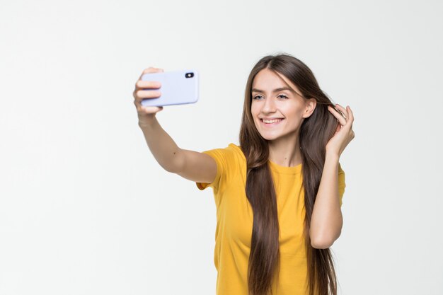 Selfie castana della presa della donna con lo Smart Phone isolato sulla parete bianca