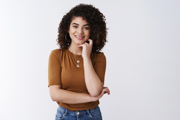 Sembra interessante. Curiosa bella sorridente felice ragazza dai capelli ricci in ascolto avere piacevole conversazione divertente tocco guancia ghignando cenno del capo d'accordo parlando collega pausa pranzo, sfondo bianco