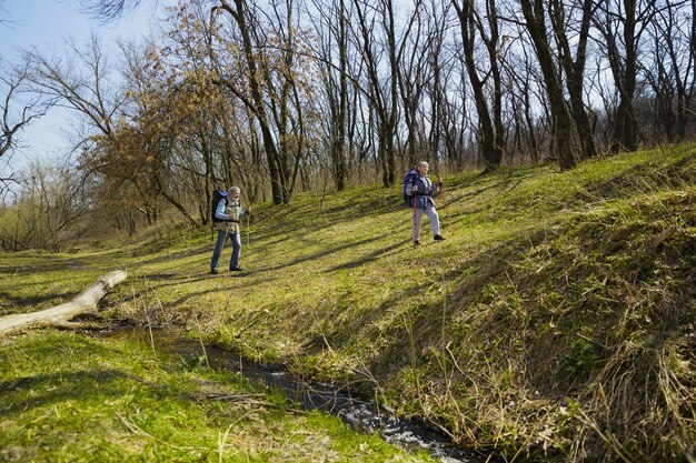 Sempre più in alto e più forte. Coppia di famiglia invecchiato dell'uomo e della donna in abito turistico che cammina al prato verde in una giornata di sole vicino al torrente