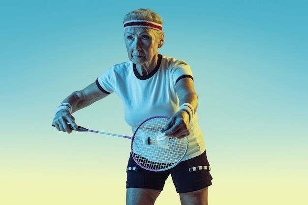 Senior donna che gioca a badminton in abbigliamento sportivo sulla parete sfumata in luce al neon