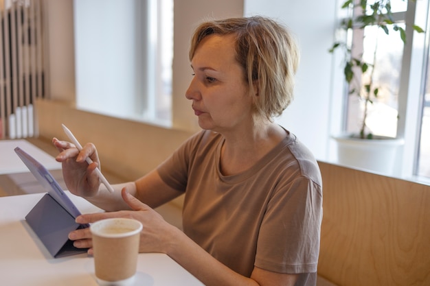 Senior donna che lavora al suo tablet in un bar