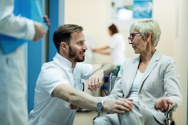 Senior donna in sedia a rotelle e metà medico adulto parlando in un corridoio in ospedale