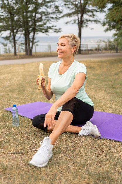 Senior donna mangiare banane all'aperto nel parco dopo lo yoga