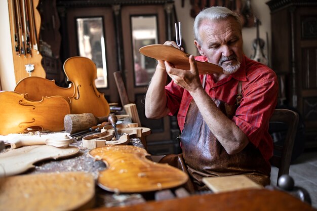 Senior falegname artigiano che controlla la qualità del suono del materiale in legno nella sua vecchia falegnameria