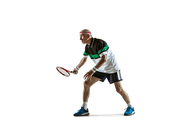 Senior uomo che indossa abbigliamento sportivo giocando a tennis isolato su sfondo bianco. Il modello maschile caucasico in ottima forma rimane attivo e sportivo. Concetto di sport, attività, movimento, benessere. Copyspace, annuncio.