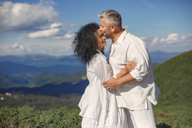 Senior uomo e donna in montagna. Coppia adulta innamorata al tramonto. Uomo in camicia bianca.