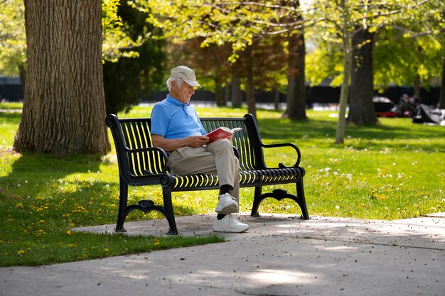 Senior uomo seduto su una panchina all'aperto e libro di lettura