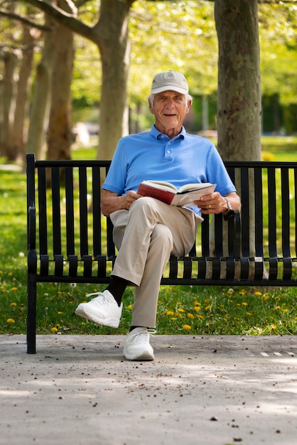 Senior uomo seduto su una panchina all'aperto e libro di lettura