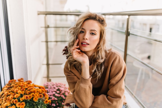 Sensuale ragazza europea che si siede alla terrazza. ritratto di donna graziosa interessata in posa accanto a fiori.