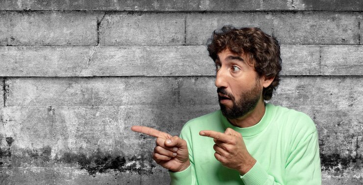 Foto gratuito sentendosi scioccato e sorpreso indicando per copiare lo spazio sul lato con sguardo a bocca aperta stupito