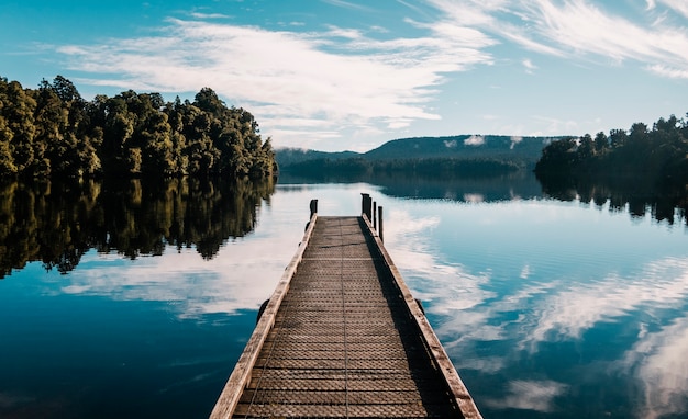 Sentiero in legno con alberi e un cielo blu riflesso sul lago Mapourika Waiho in Nuova Zelanda