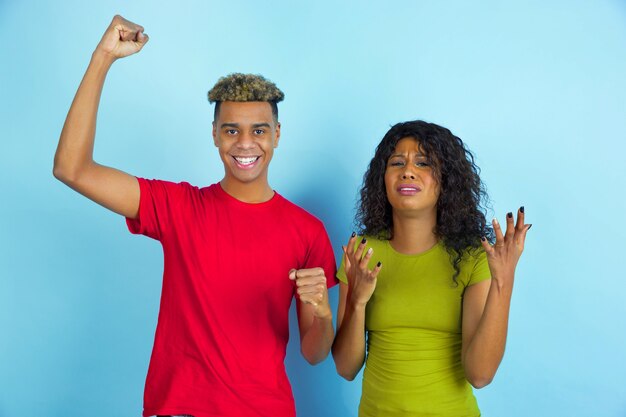 Sentimenti tristi e felici. Giovane uomo afro-americano emotivo e donna in abiti casual in posa su sfondo blu. Bella coppia. Concetto di emozioni umane, espansione facciale, relazioni, annuncio.