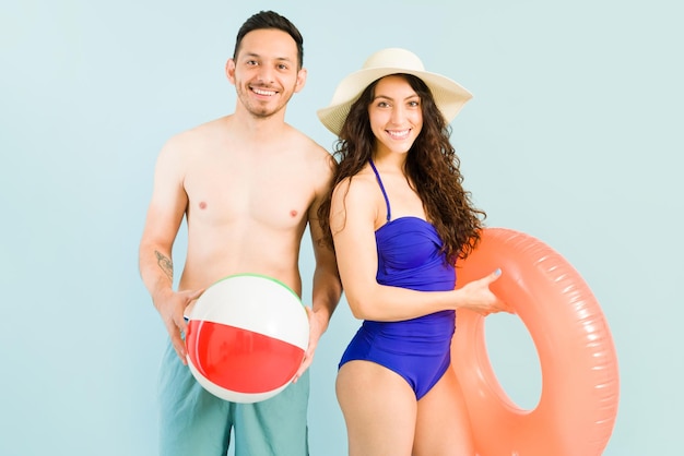 Sentirsi felici e rilassati durante il nostro viaggio di vacanza. Giovane uomo latino e donna caucasica in costume da bagno pronto per andare in spiaggia con un bagnino gonfiabile e un pallone da spiaggia