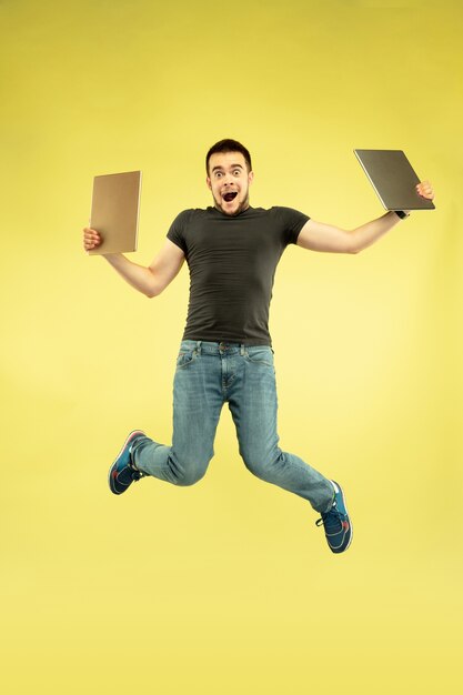 Senza peso. Ritratto integrale dell'uomo felice di salto con i gadget isolati su colore giallo.