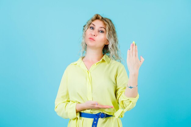 Seriamente donna bionda sta mostrando la sua mano alla fotocamera su sfondo blu