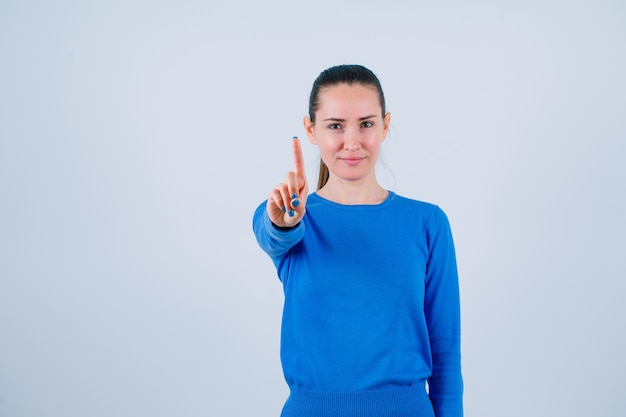 Seriamente giovane ragazza sta mostrando un gesto minuto su sfondo bianco