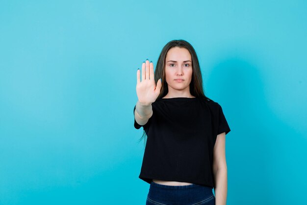 Seriamente, la ragazza sta mostrando il gesto di arresto estendendo la mano alla fotocamera su sfondo blu