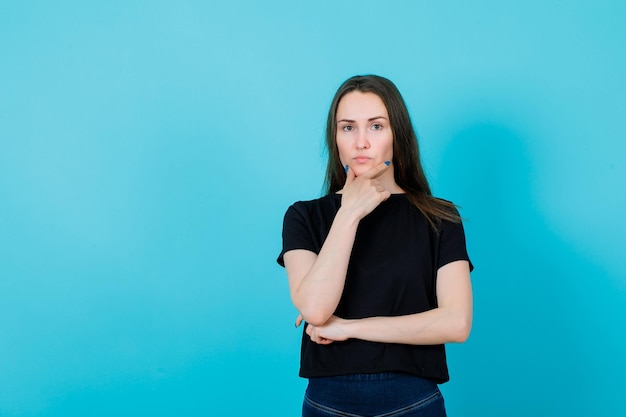 Seriamente la ragazza sta pensando mettendo la mano sul mento su sfondo blu