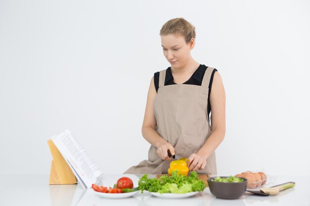 Serio donna lettura libri di ricetta durante la cottura