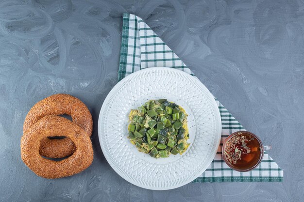 Servire legumi di fagioli cotti con le uova, accanto a una tazza di tè e due bagel su una superficie di marmo.