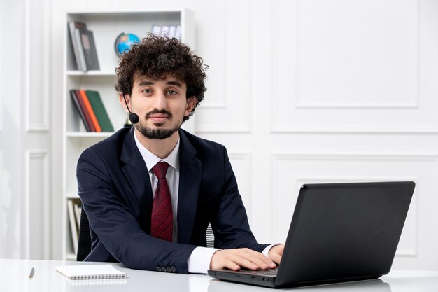 Servizio clienti bel ragazzo in tuta da ufficio con laptop e auricolare serio e concentrato