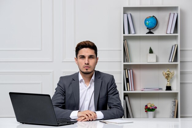 Servizio clienti bel ragazzo intelligente con laptop in giacca da ufficio grigio che sembra molto serio