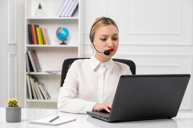 Servizio clienti bella ragazza carina in camicia bianca con computer e auricolare digitando