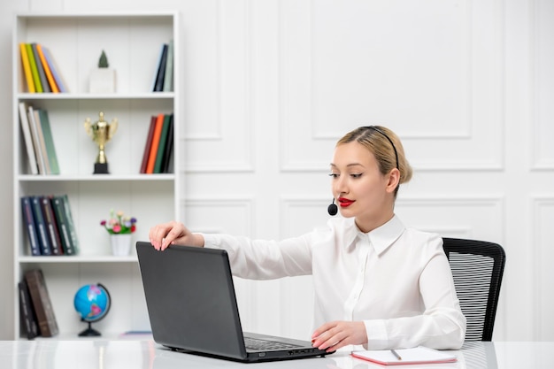 Servizio clienti camicia da ufficio ragazza bionda carina con auricolare e computer portatile di chiusura