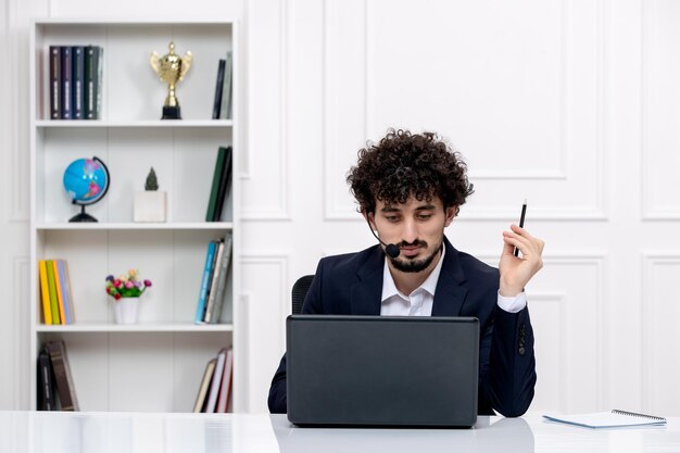 Servizio clienti carino ragazzo bruna in abito da ufficio con computer e auricolare tenendo la penna