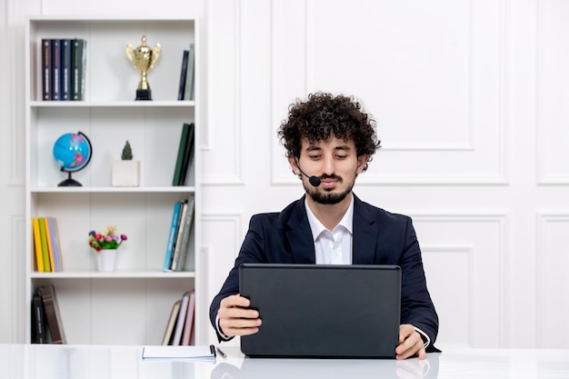 Servizio clienti carino ragazzo bruna in abito da ufficio con computer portatile e auricolare toccando il computer